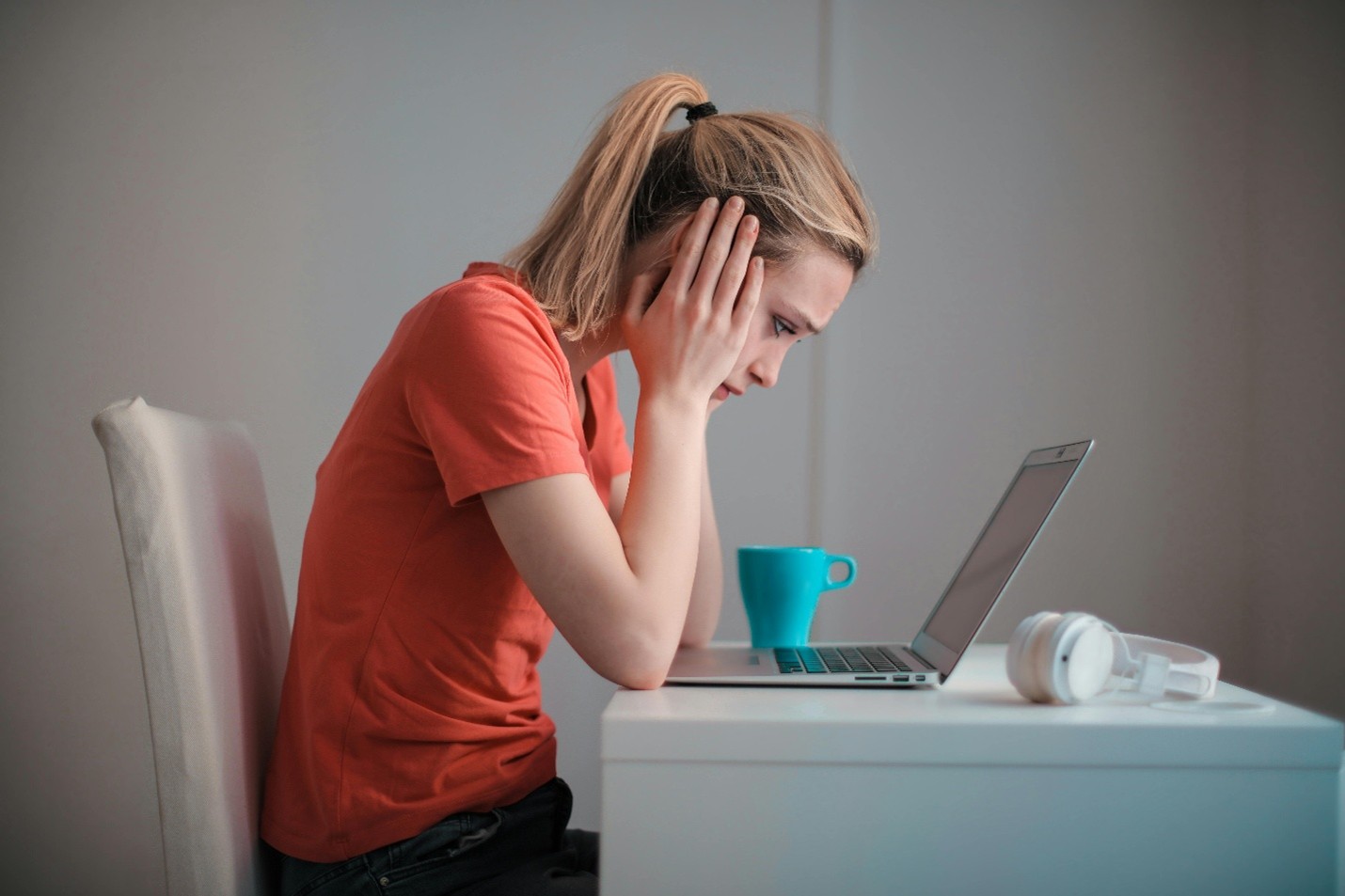 Frustrated young woman sitting at a desk with a laptop, feeling stuck during her job search